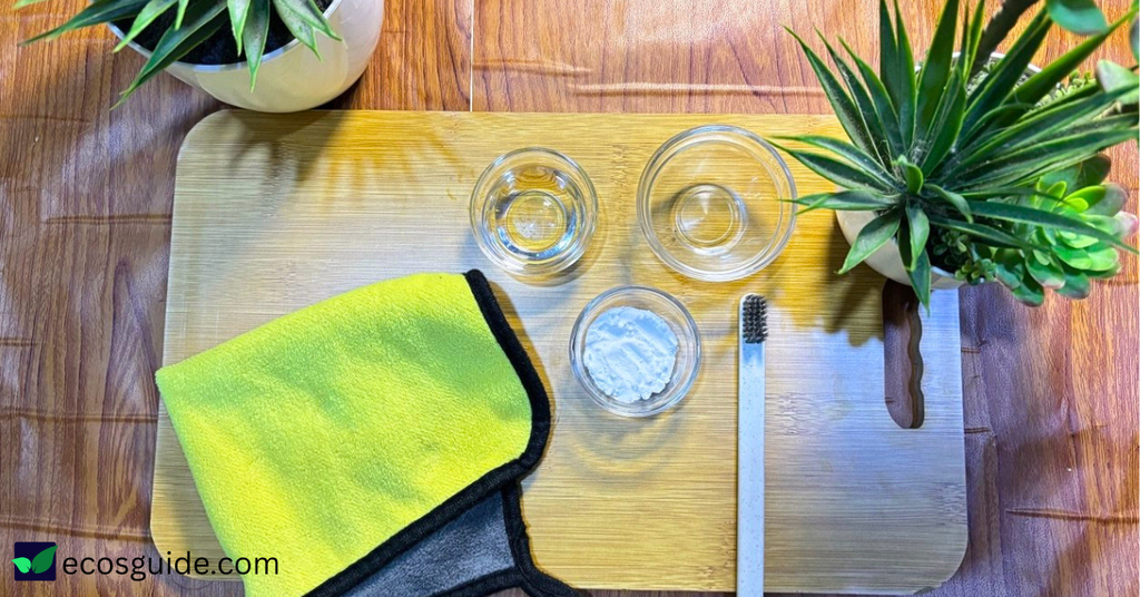 The ingredients I use to clean a dishwasher with vinegar and baking soda — a bowl of vinegar, baking soda, a microfiber cloth, and an old toothbrush laid out on a wooden board.